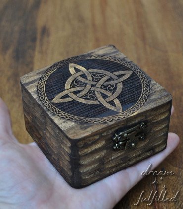 a hand holds a small dark wooden box engraved with a witch symbol