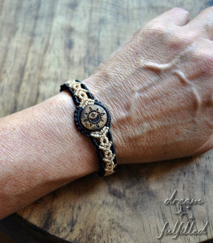 top view of a black and beige thread bracelet with wood engraved with symbols of the sun, moon, and star