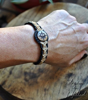 muñeca muestra pulsera trenzada de color negro y beis con pieza de madera grabada con sol, luna y estrella