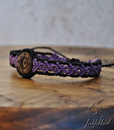 mano sujeta pulsera de hilo trenzado de color negro y morado y madera grabada laser con símbolo de sol luna y estrella