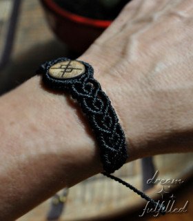 vista lateral de muñeca con una pulsera de madera e hilo de macramé negro, grabada con bindrune de amor eterno