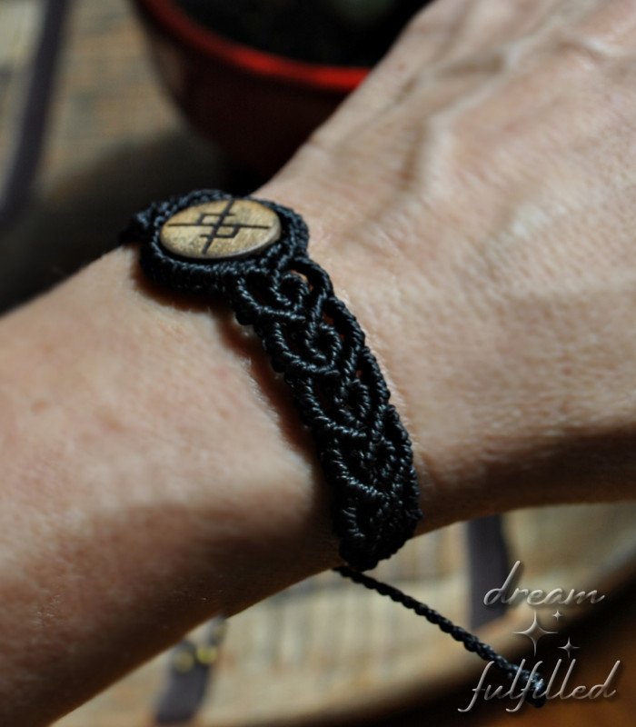 vista lateral de muñeca con una pulsera de madera e hilo de macramé negro, grabada con bindrune de amor eterno