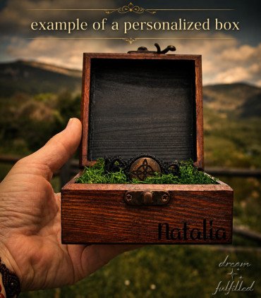 una mano sostiene una caja de madera que contiene pulsera de madera y macramé grabada con símbolo