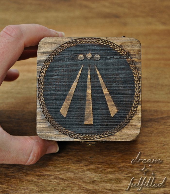 Dark wooden box with engraved Awen symbol in center and metal latch, top view showing details of engraving.