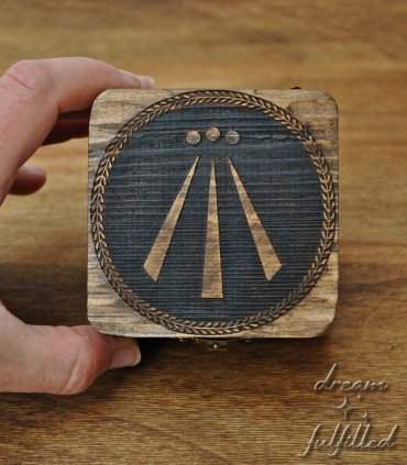 Dark wooden box with engraved Awen symbol in center and metal latch, top view showing details of engraving.