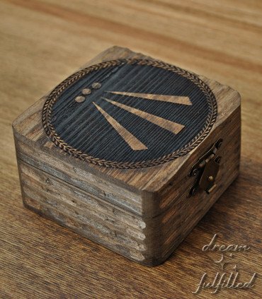 Caja de madera oscura con tapa grabada con símbolo Awen central y cierre metálico, vista superior mostrando detalle del grabado.