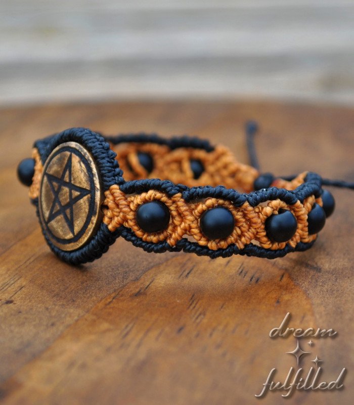 An orange and black macramé bracelet with intertwined matte black onyx beads, engraved with the pentacle symbol