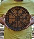 a person holds a large wooden plate engraved with the Viking symbol of the vegvisir
