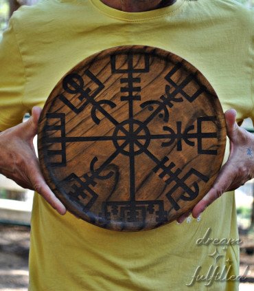 una persona sostiene un plato grande de madera grabado con el símbolo vikingo del vegvisir