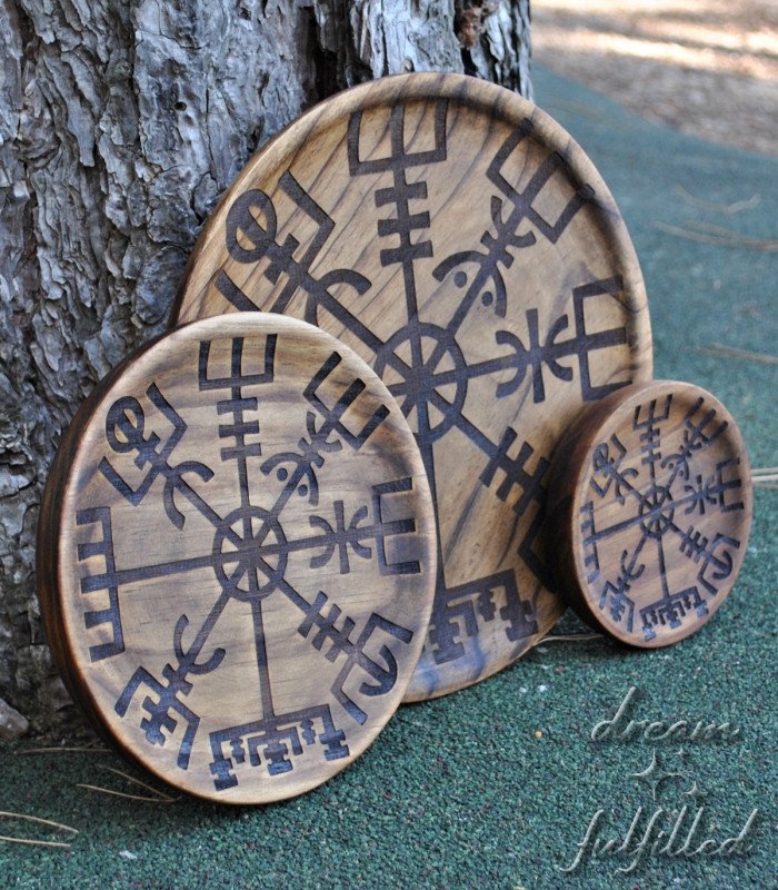 tres platos de madera de diferentes tamaños grabados con el vegvisir, apoyados sobre un árbol