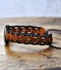 Side view of a brown wooden and braided thread bracelet, engraved with the scallop shell symbol of the Camino de Santiago.